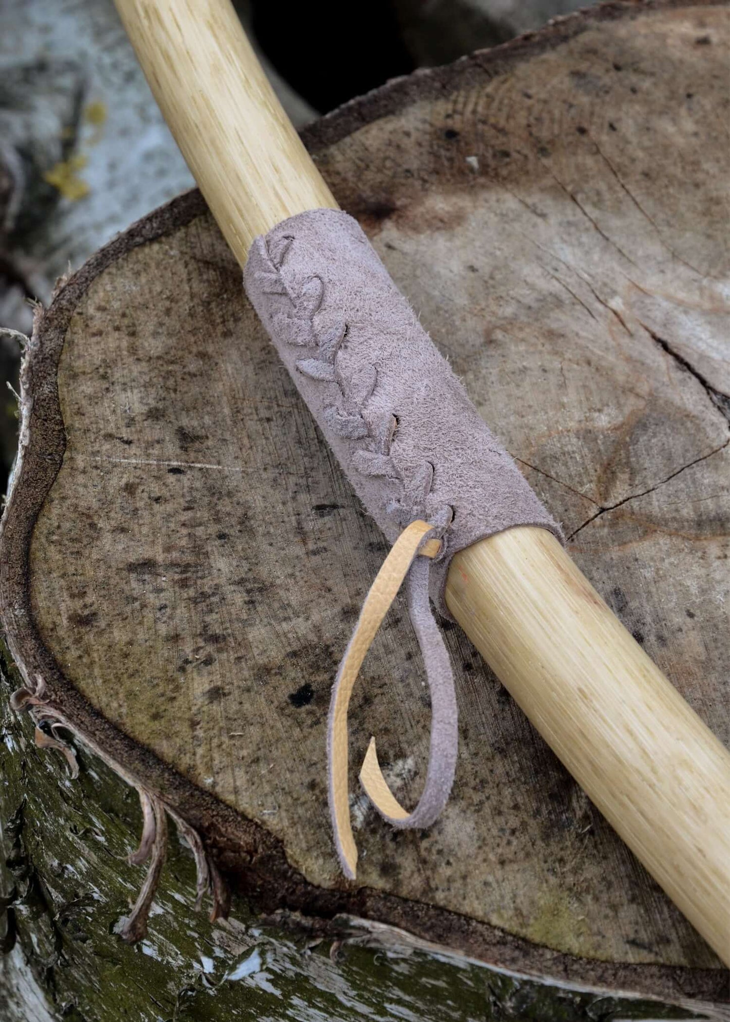 Detail of a handcrafted longbow grip with leather lacing on a wood background.