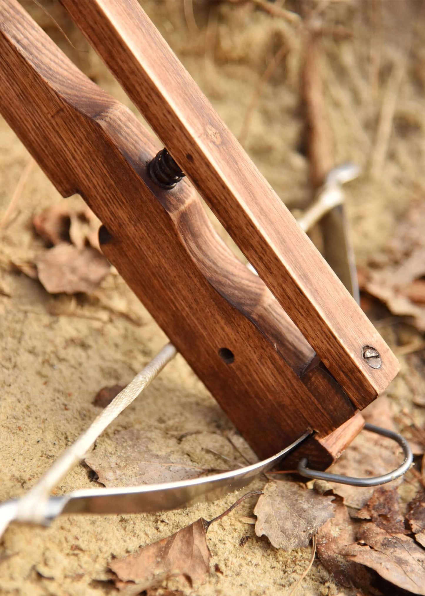 Detailaufnahme einer funktionalen Mini Armbrust aus Holz auf dem Boden mit Laub.