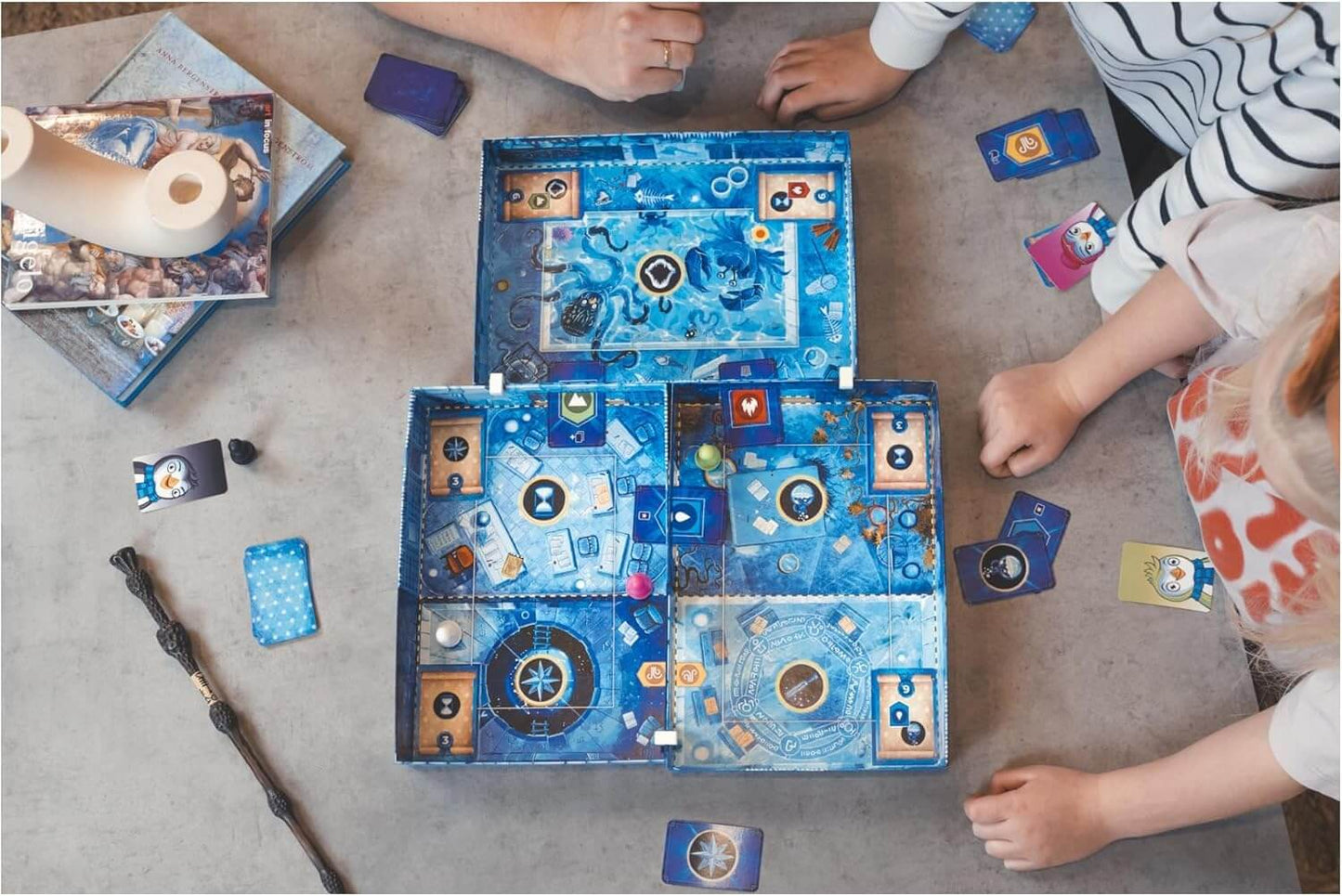 Spielende Familie mit dem Ice Cool Wizards Brettspiel, blaues Design, Karten und Spielfiguren auf dem Tisch.